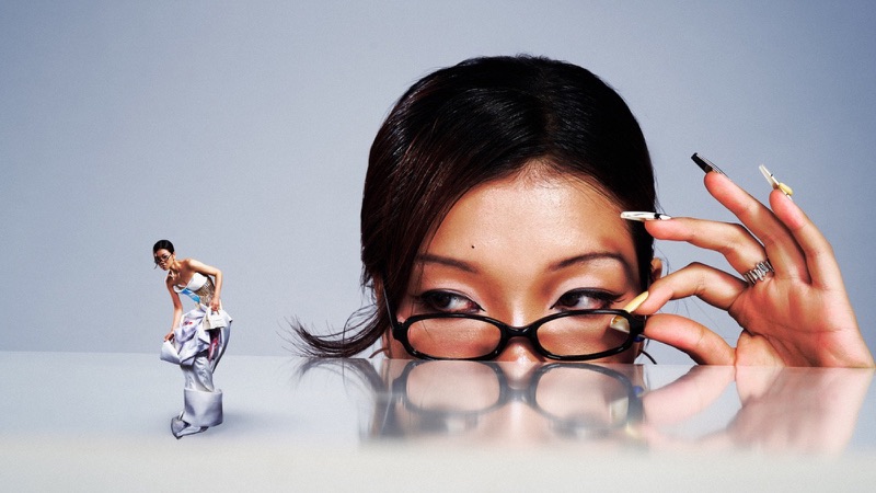 Surreal editorial composite of a giant bespectacled face beside the model, keyboard-key manicure visible