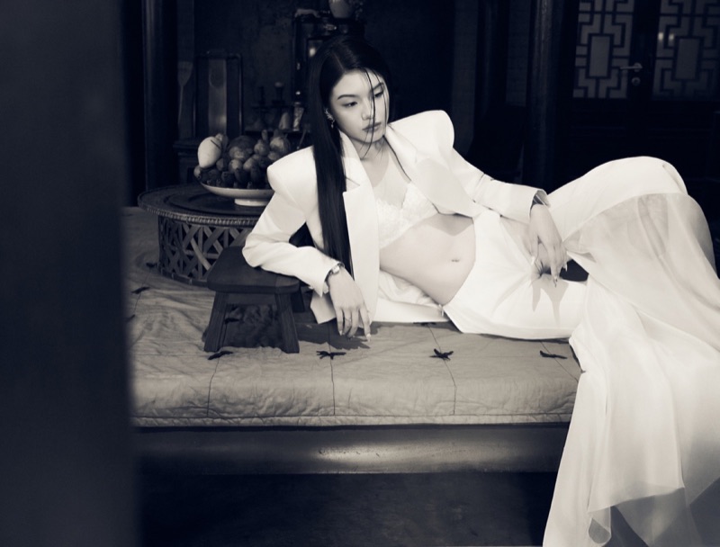 Black-and-white reclining editorial on the daybed in a strong-shouldered blazer with a soft skirt